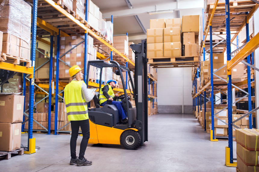 Lagerarbete, en person kör truck med stor last och en står bredvid